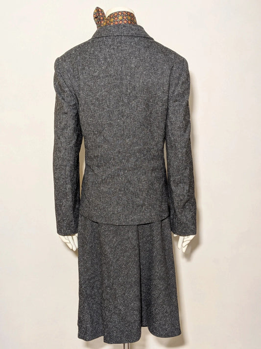 Anisette grey skirt suit with three-button blazer and knee-length skirt, tweed texture.