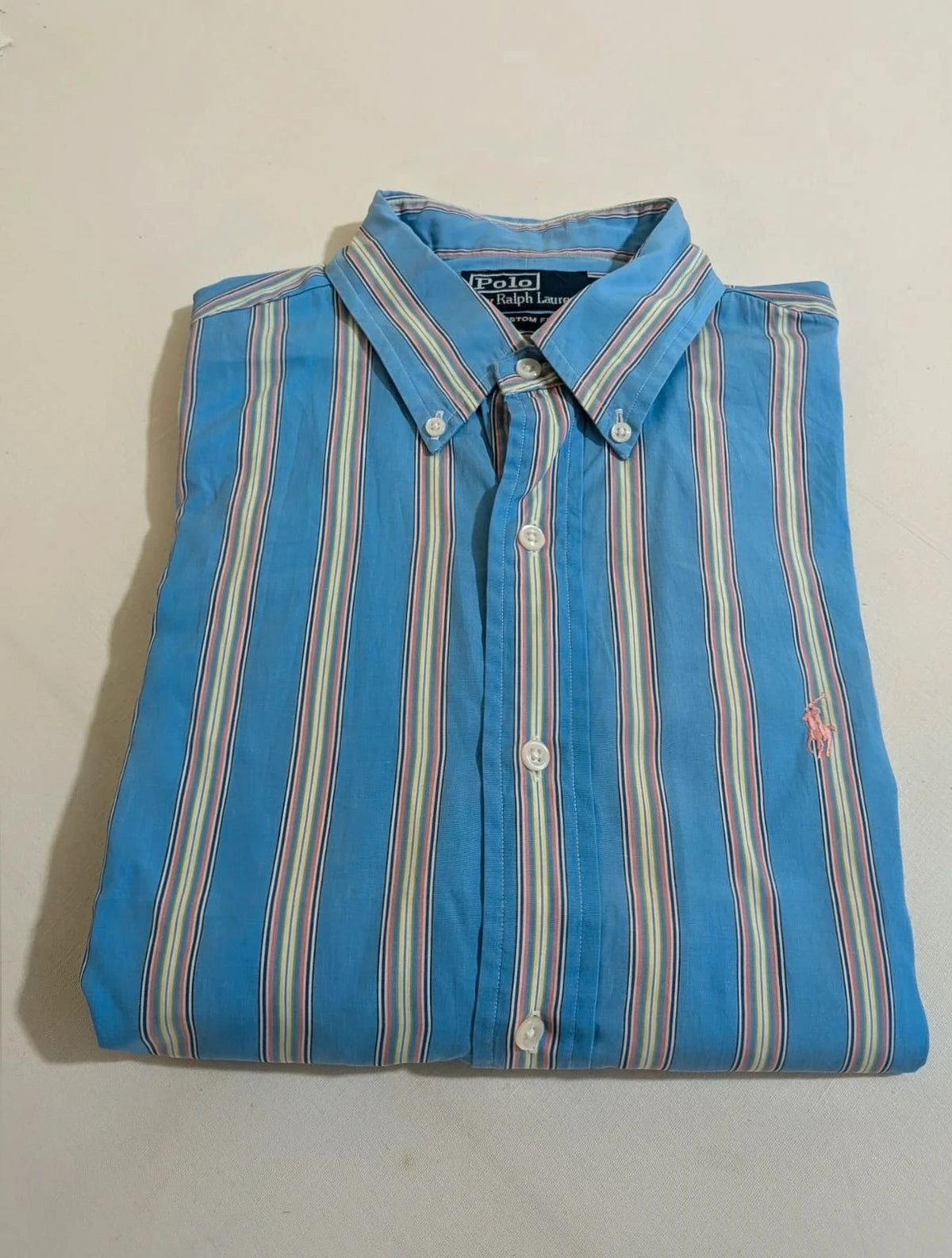 Polo Ralph Lauren multicolor striped shirt with pink pony logo on sky blue background.