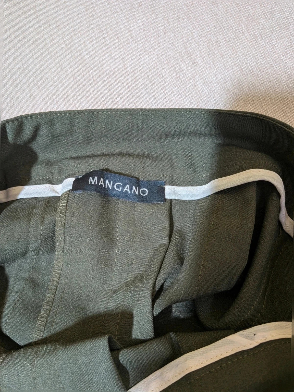 Mangano green military skirt suit with elegant front pleats and metallic ring detail.
