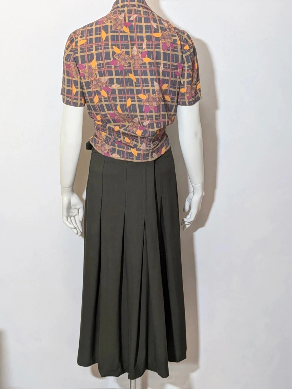 Mangano green military skirt suit with elegant front pleats and metallic ring detail.