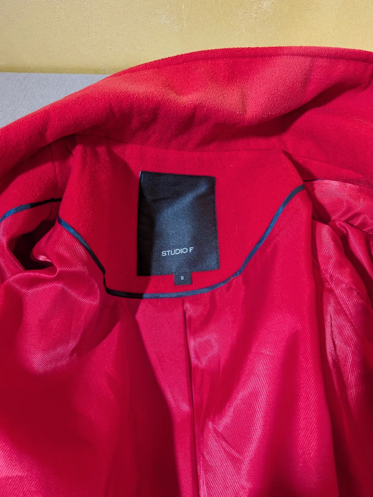 Studio F red coat with black button closure and gold logo tag on collar.