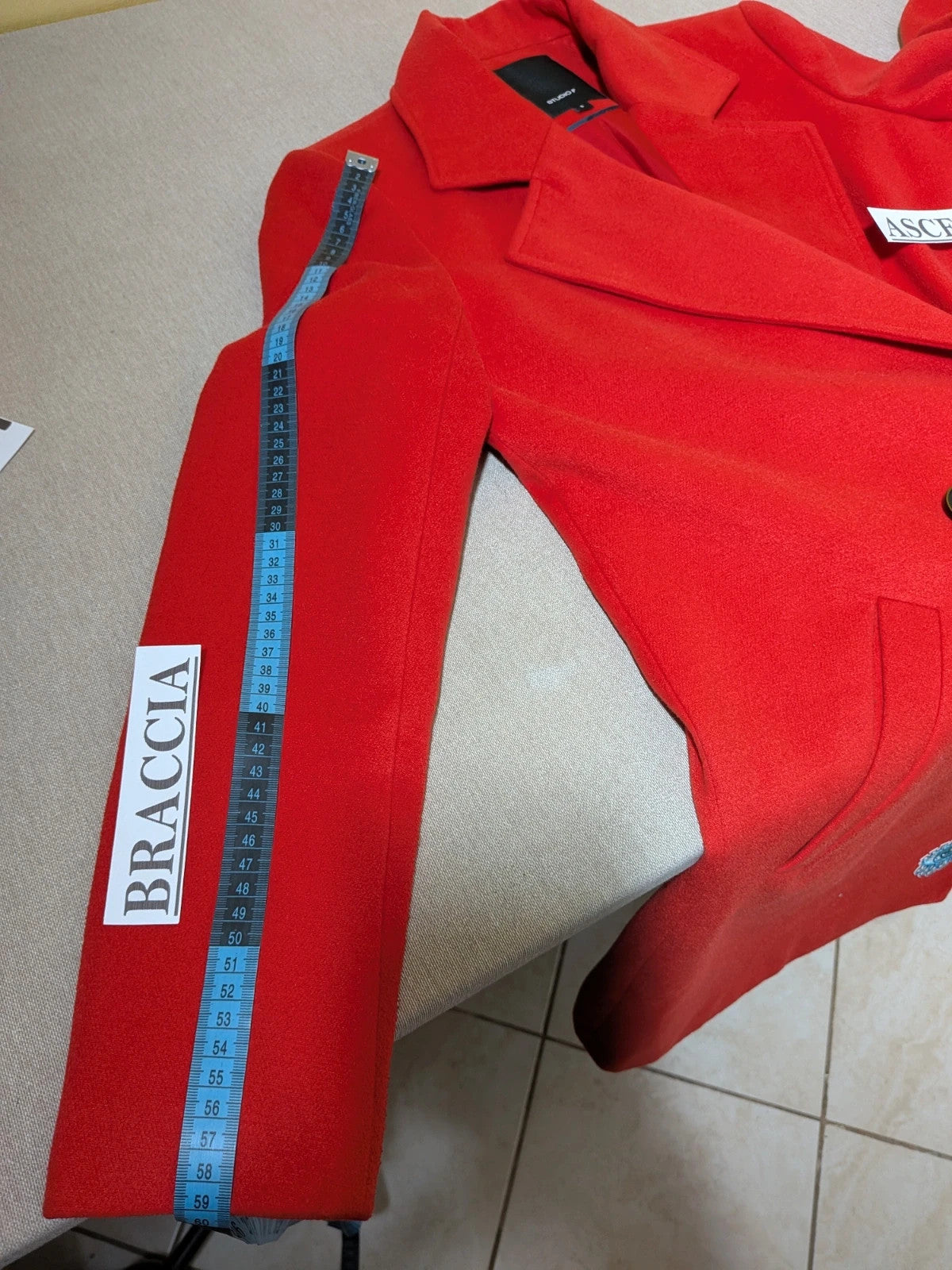 Studio F red coat with black button closure and gold logo tag on collar.
