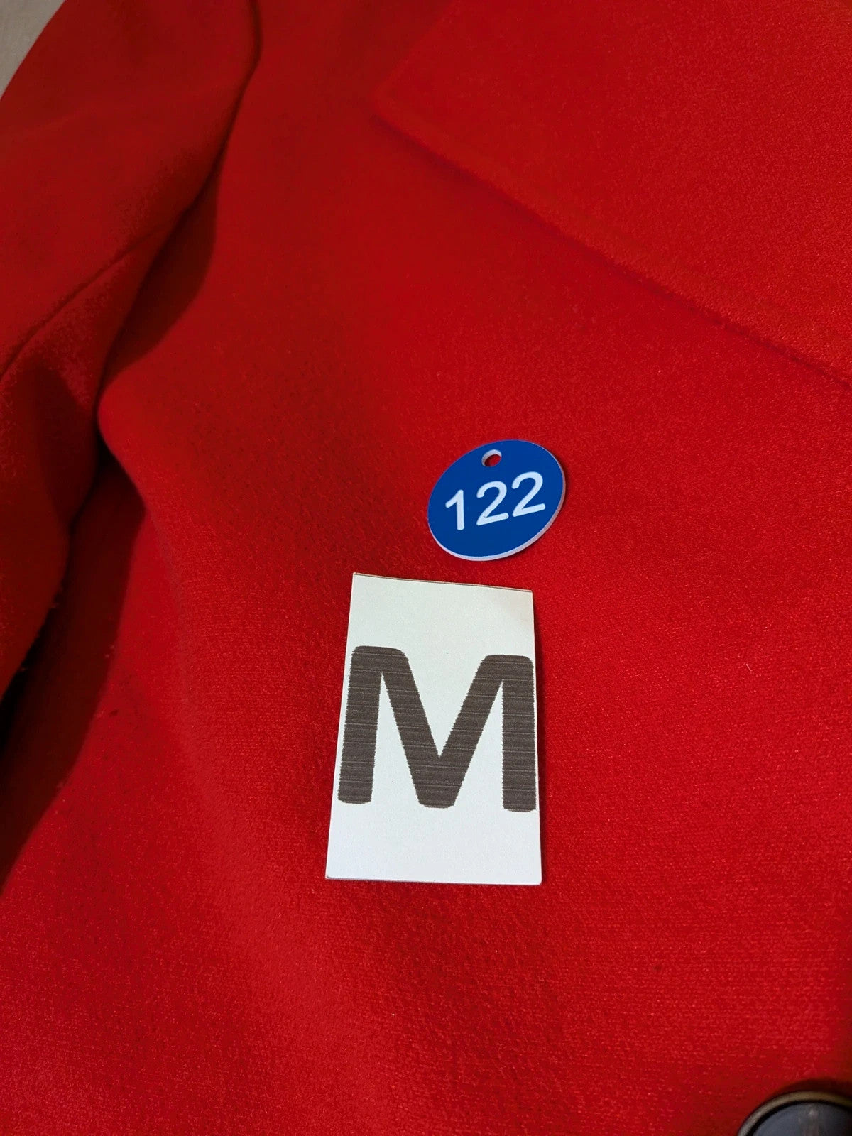 Studio F red coat with black button closure and gold logo tag on collar.