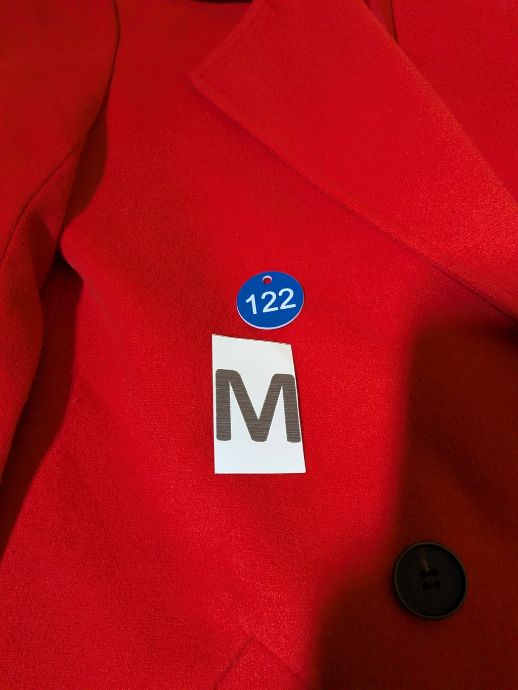 Studio F red coat with black button closure and gold logo tag on collar.