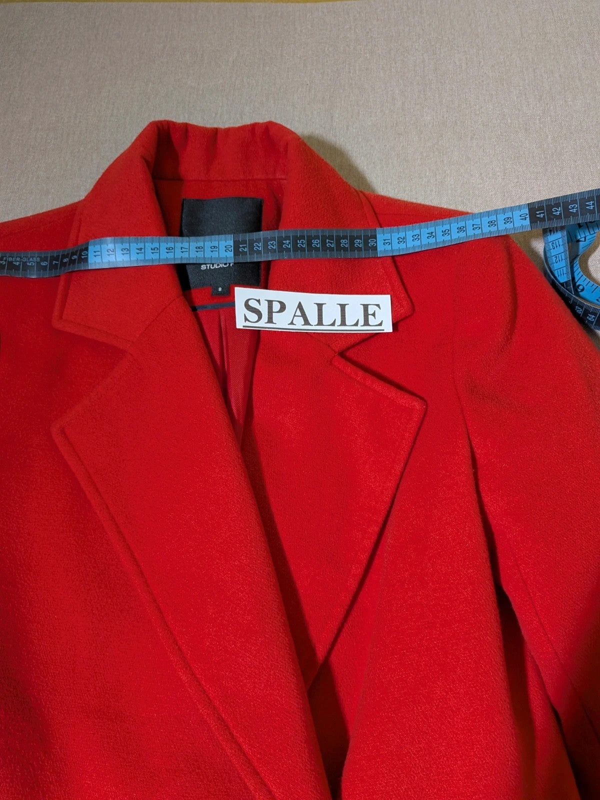 Studio F red coat with black button closure and gold logo tag on collar.