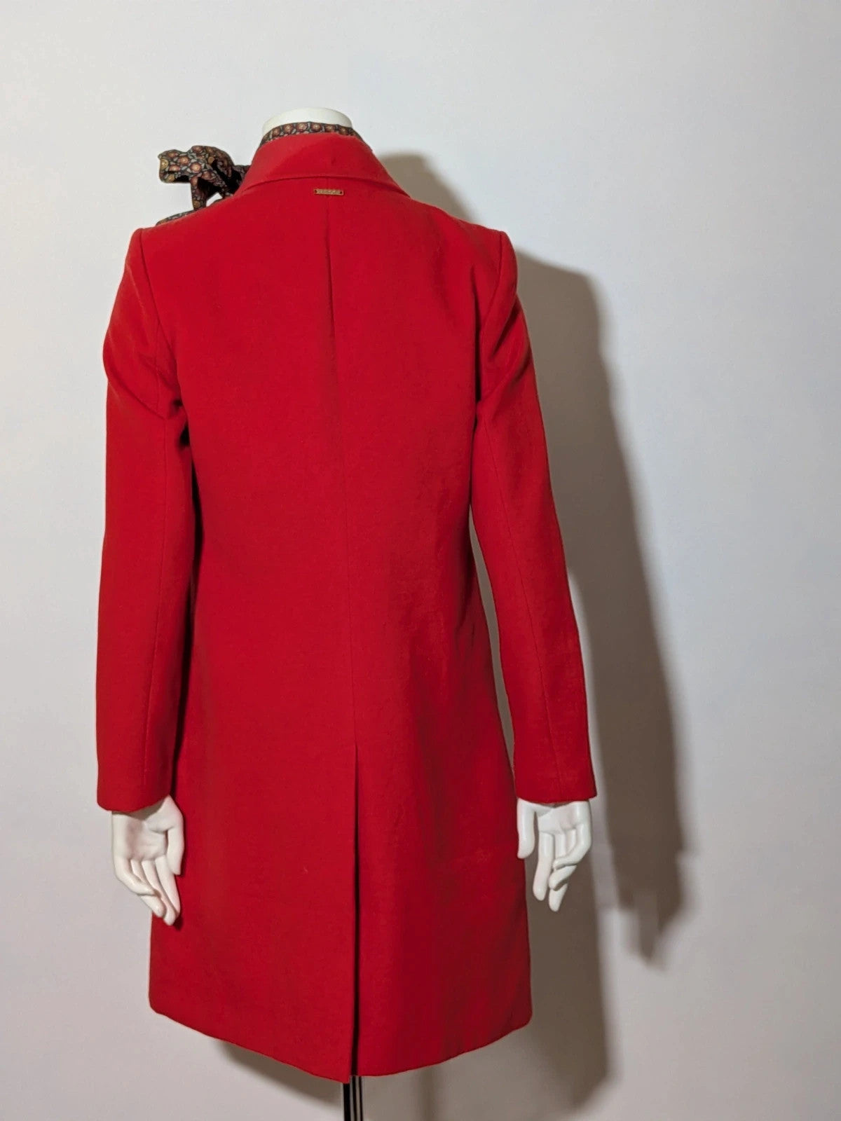 Studio F red coat with black button closure and gold logo tag on collar.