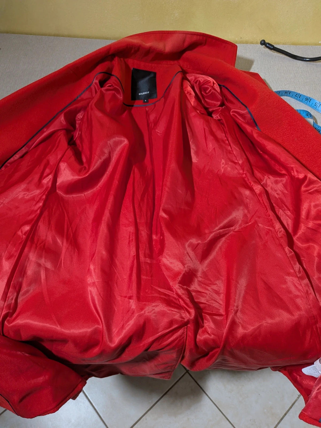 Studio F red coat with black button closure and gold logo tag on collar.