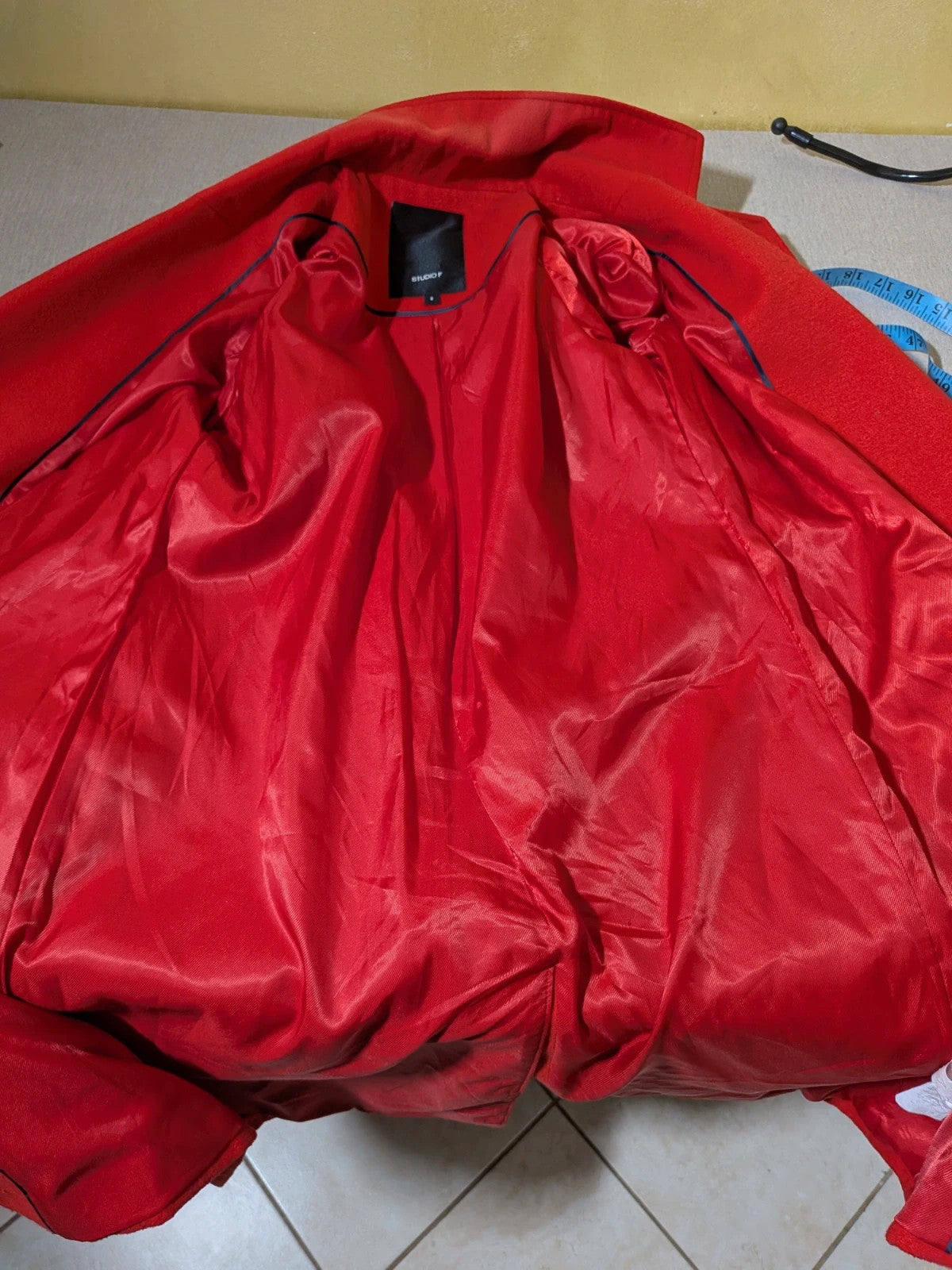 Studio F red coat with black button closure and gold logo tag on collar.