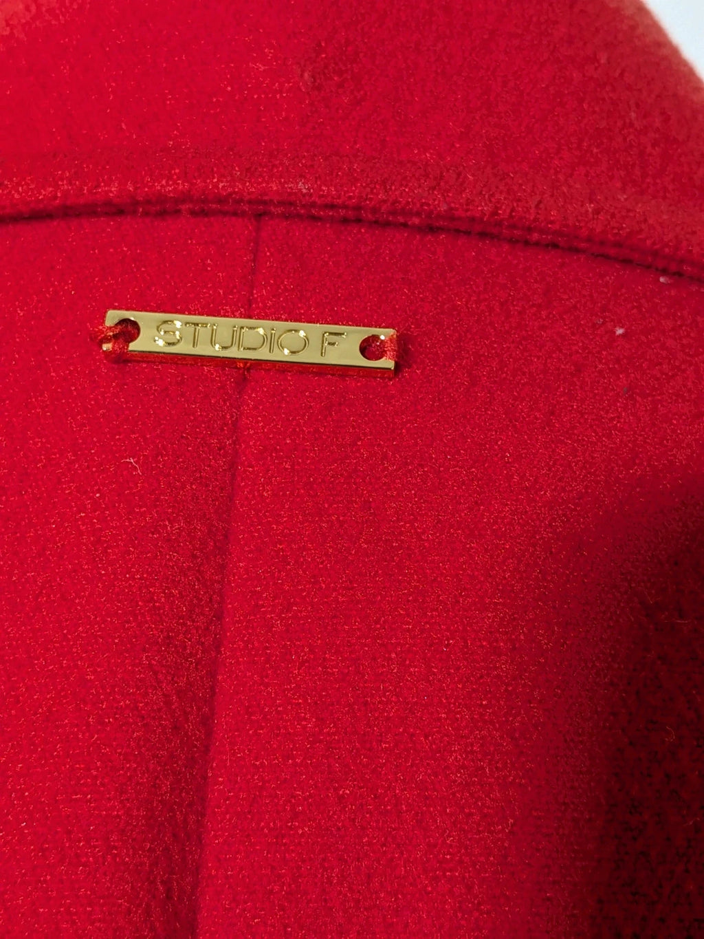 Studio F red coat with black button closure and gold logo tag on collar.