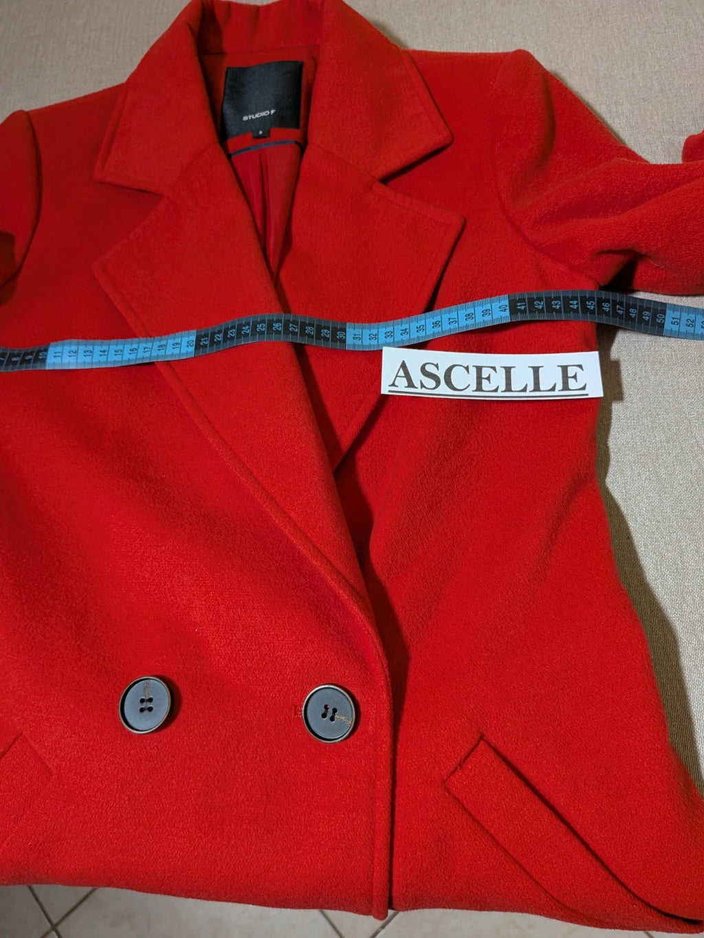 Studio F red coat with black button closure and gold logo tag on collar.