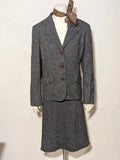 Anisette grey skirt suit with three-button blazer and knee-length skirt, tweed texture.