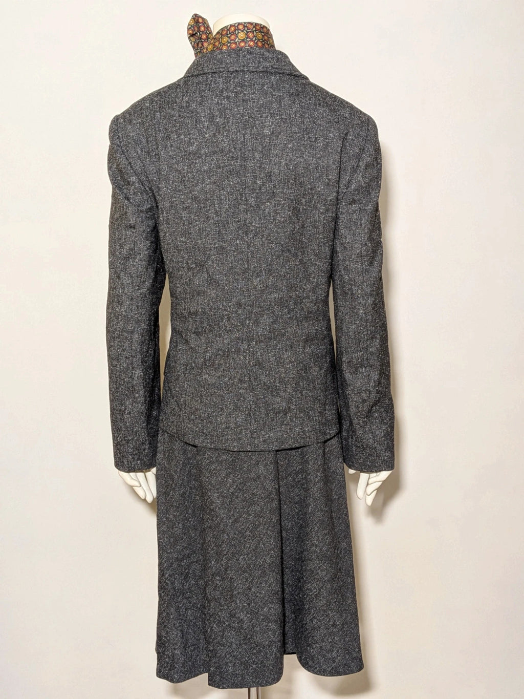 Anisette grey skirt suit with three-button blazer and knee-length skirt, tweed texture.
